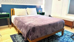 Un dormitorio con una cama de madera, una pared con diseño azul y blanco, una mesita de noche verde y una alfombra azul.