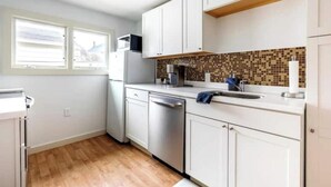 Een moderne keuken met witte kastjes, een betegelde achterwand en een vaatwasser.