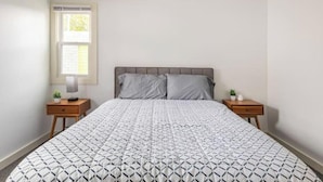 Een slaapkamer met een bed, twee nachtkastjes, een raam en uitzicht op bomen.