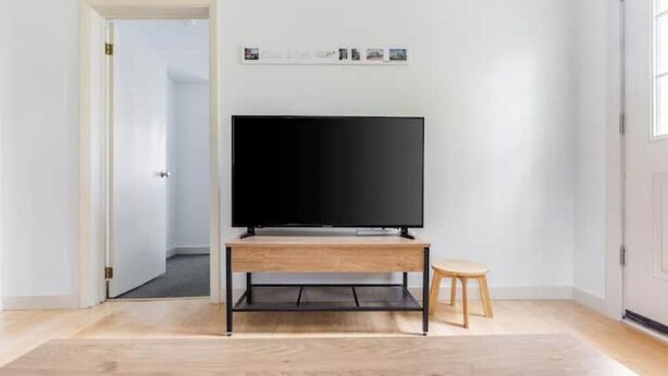 Een kamer met een televisie op een houten standaard, een klein krukje, en een deur naar een andere ruimte.