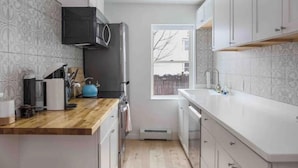 A compact kitchen with white cabinets, a wooden countertop, a black range hood, and a window providing a view of the outside. - Petite+Perfect Modern Pad: parking+laundry+yard (Burlington)