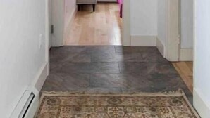 A narrow hallway with a patterned rug, a bench, and a door leading to a room with a window. - Petite+Perfect Modern Pad: parking+laundry+yard (Burlington)