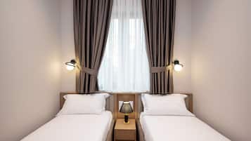 Camera d'albergo con due letti singoli, un comodino con una lampada e tende.