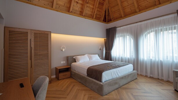 Un dormitorio con techo de madera, una cama con ropa blanca, una mesita de noche, un escritorio y una silla.