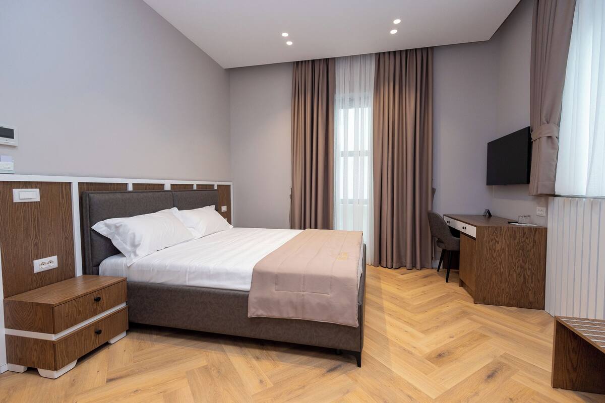 A modern hotel room with a bed, wooden nightstands, a desk, and a TV.