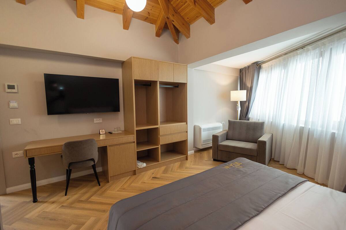 A modern hotel room with a wooden desk, a flat-screen TV, a comfortable armchair, and a large bed.
