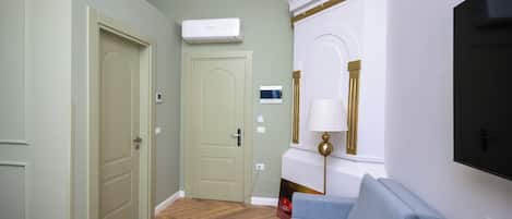 A room with a wooden herringbone floor, a light green door, a white air conditioning unit, a grey sofa, and a flat-screen TV mounted on the wall.