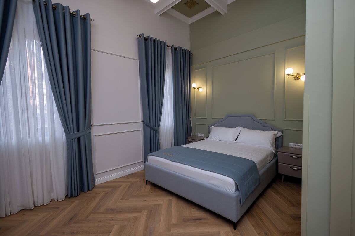 A bedroom with a bed, nightstands, a mirror, and curtains.