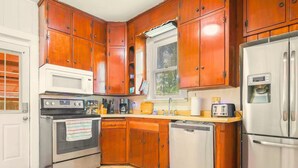 Eine kompakte Küche mit Holzschränken, einem Edelstahlkühlschrank, einer Mikrowelle, einem Backofen und einem Geschirrspüler.