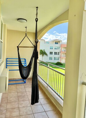 Un balcon avec un fauteuil suspendu, un banc bleu et une vue sur un immeuble d’habitation.