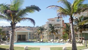 A pool area with lounge chairs and palm trees, surrounded by buildings with balconies. - #4 Beach Apt 2BR, 2BA - Jobos, Montones, Shacks (Isabela)