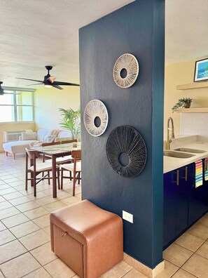 A modern kitchen with a dark blue accent wall, a dining area with a table and chairs, and a ceiling fan. - #4 Beach Apt 2BR, 2BA - Jobos, Montones, Shacks (Isabela)