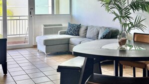 A modern living room with a sectional sofa, a glass-top dining table, and a ceiling fan. - #4 Beach Apt 2BR, 2BA - Jobos, Montones, Shacks (Isabela)