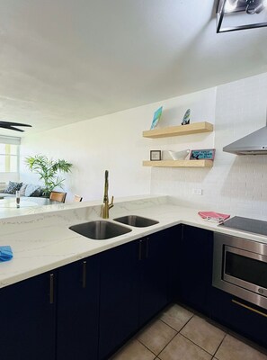 A modern kitchen with dark cabinets, a white countertop, two sinks, a stainless steel oven, and wooden shelves above the countertop.