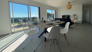 A modern dining area with a large table, white chairs, and a view of a balcony with outdoor furniture.