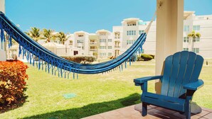 A hammock and a blue Adirondack chair on a patio with a view of a hotel building. - #6 First floor 3br, 2ba Apartment @ Jobos Beach (Isabela)