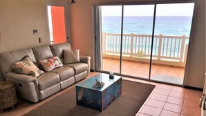 A living room with a sofa, a coffee table, and a view of the ocean through a sliding glass door. - #17 REAL Beachfront 3BR Retreat @ Isabela Beach Ct (Isabela)