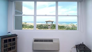 A room with a large window offering a view of the beach and a wooden structure. There is a wall-mounted air conditioner and a small cabinet with glass doors. - #3 REAL Oceanfront Ground Floor Apt @ Jobos Beach (Isabela)