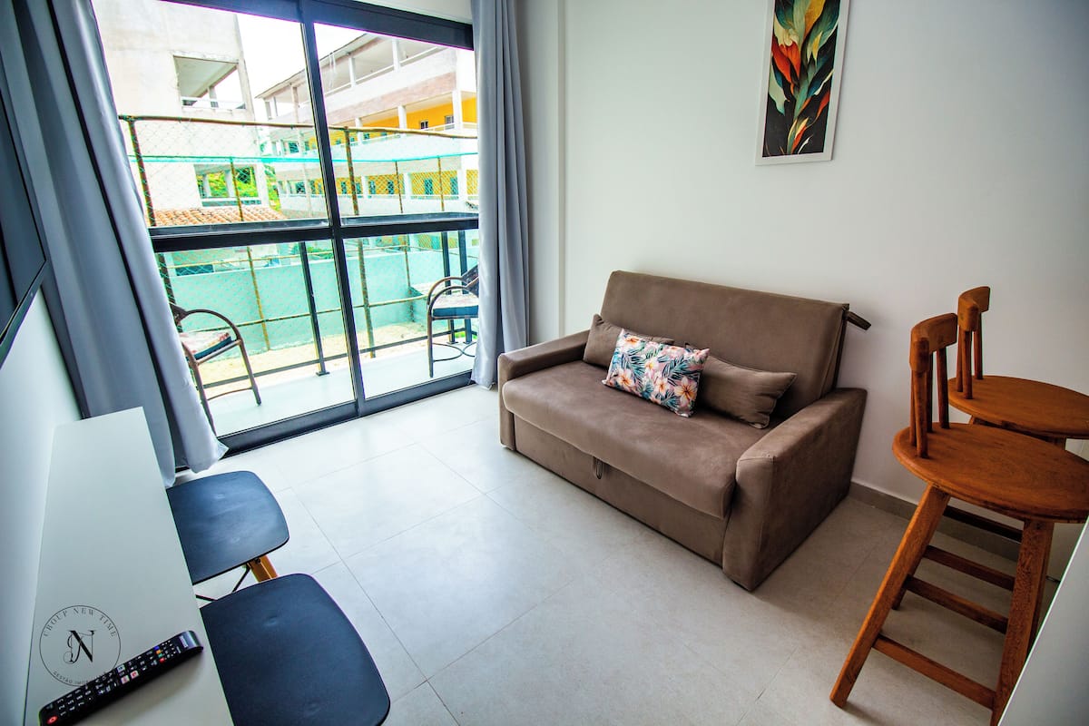 A room with a sofa, a wooden chair, a desk with a remote control, and a view of a pool through a glass door.