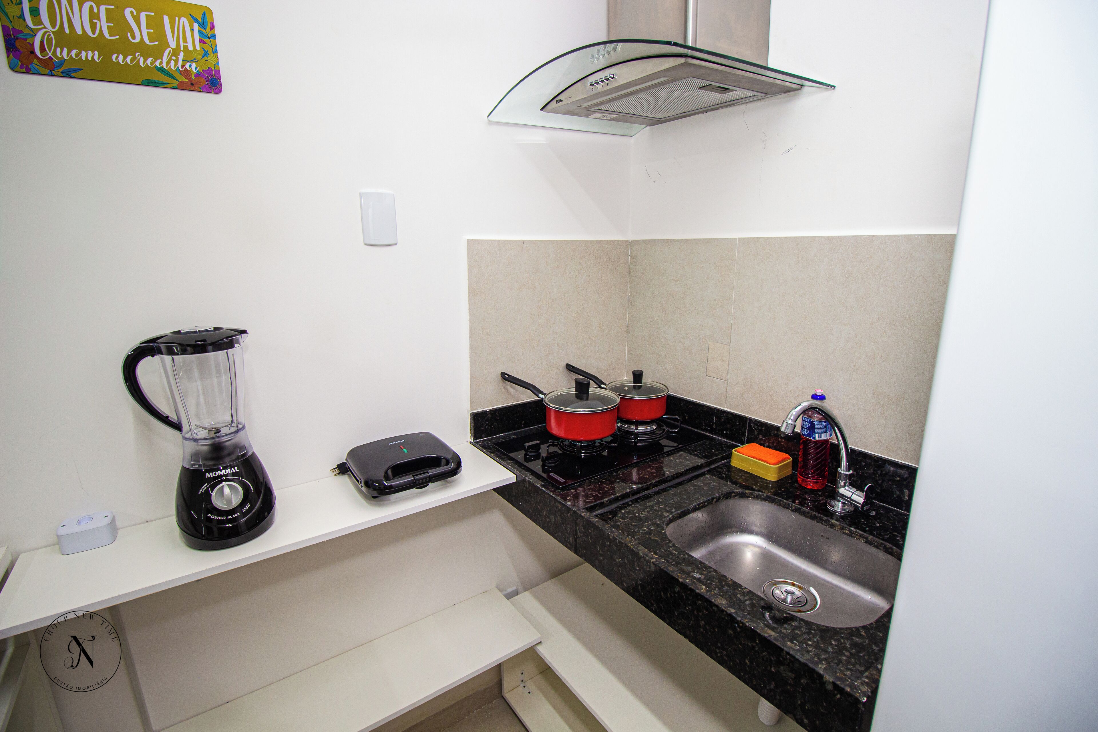 A compact kitchen with a blender, a toaster, a stove with pots, and a sink.
