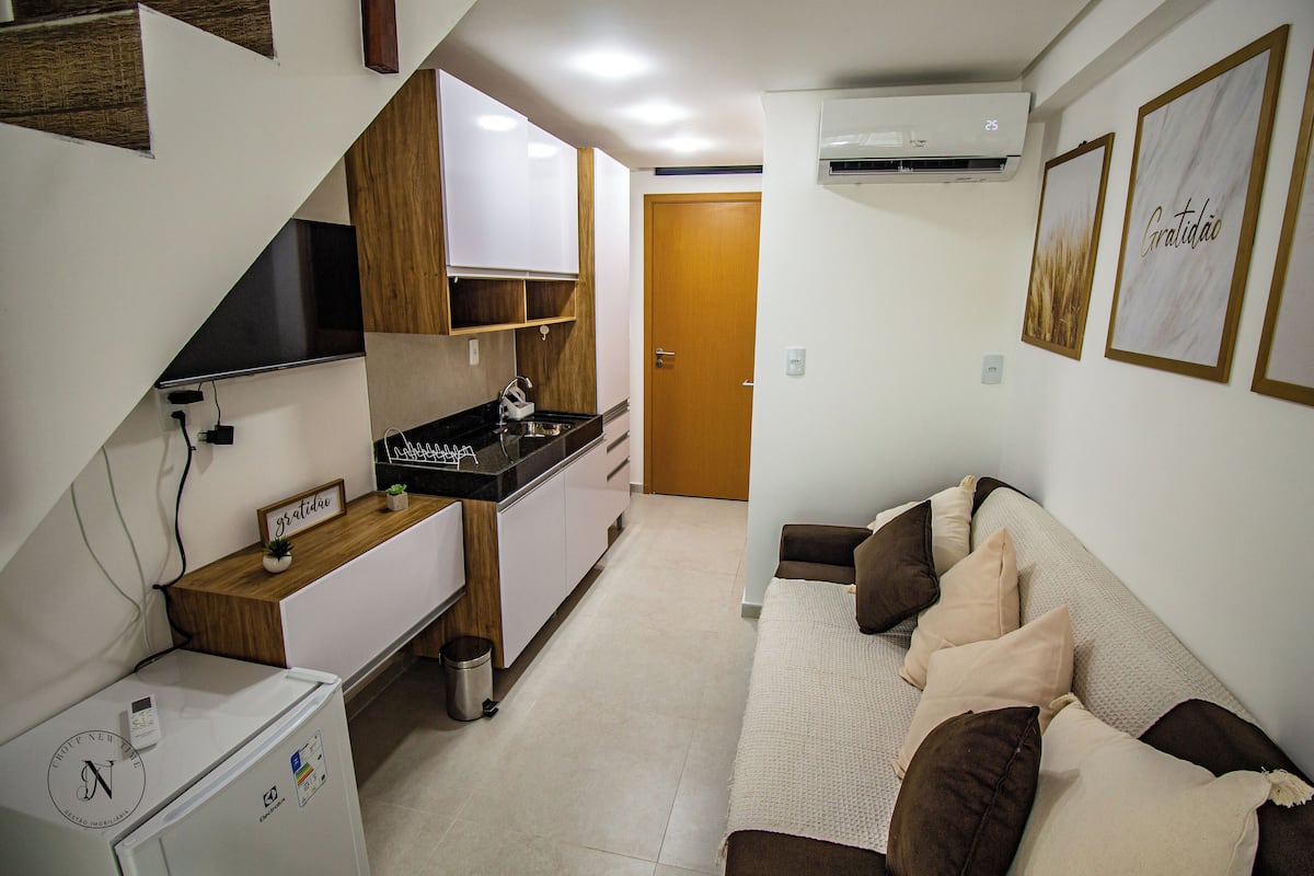 A compact living space with a kitchenette, a sofa with cushions, and a door leading to another room.