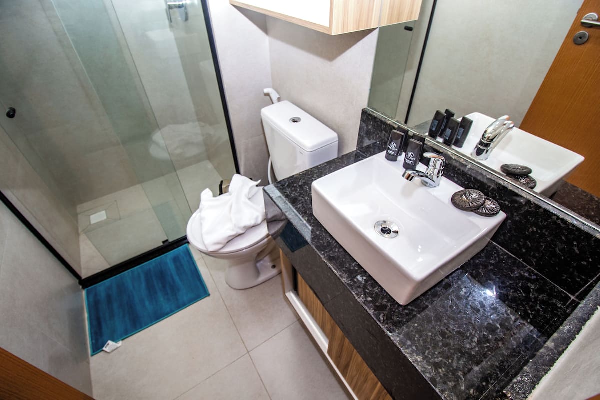 A modern bathroom with a glass shower enclosure, a white toilet, a sink with a black countertop, and a mirror above the sink.