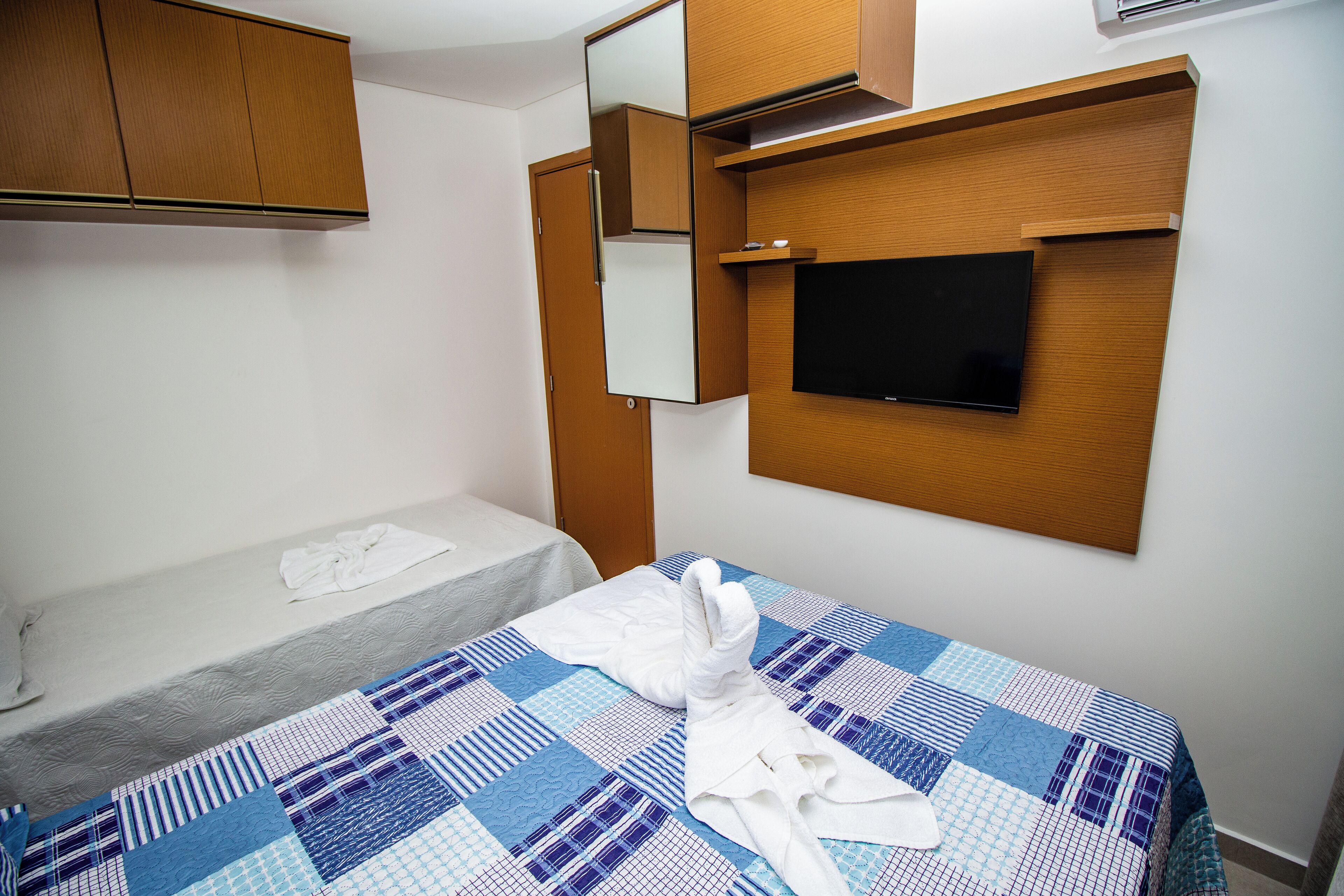 Habitación de hotel con cama, televisor montado en la pared, armario de madera y espejo.