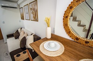 Una sala de estar moderna con una mesa de comedor de madera, un florero con plantas secas y un espejo grande con un marco de madera original.