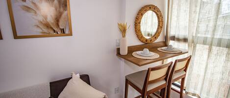 A room with a wooden dining table, two chairs, a mirror, and a framed artwork on the wall.