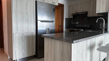Een moderne keuken met kastjes met houttextuur, een roestvrijstalen koelkast, granieten werkbladen en een roestvrijstalen spoelbak.