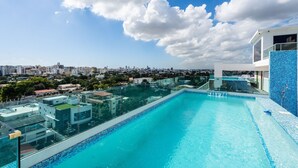 Une piscine à débordement située sur le toit, offrant une vue sur la ville et entourée d’immeubles modernes.