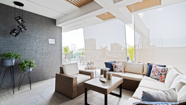 Un espace de vie extérieur moderne, avec des meubles en osier, un mur en briques grises et des plantes en pot.