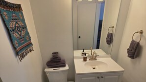 A bathroom with a white sink, a toilet, a mirror, and a patterned rug on the floor. - Southwest Motel (Grants)