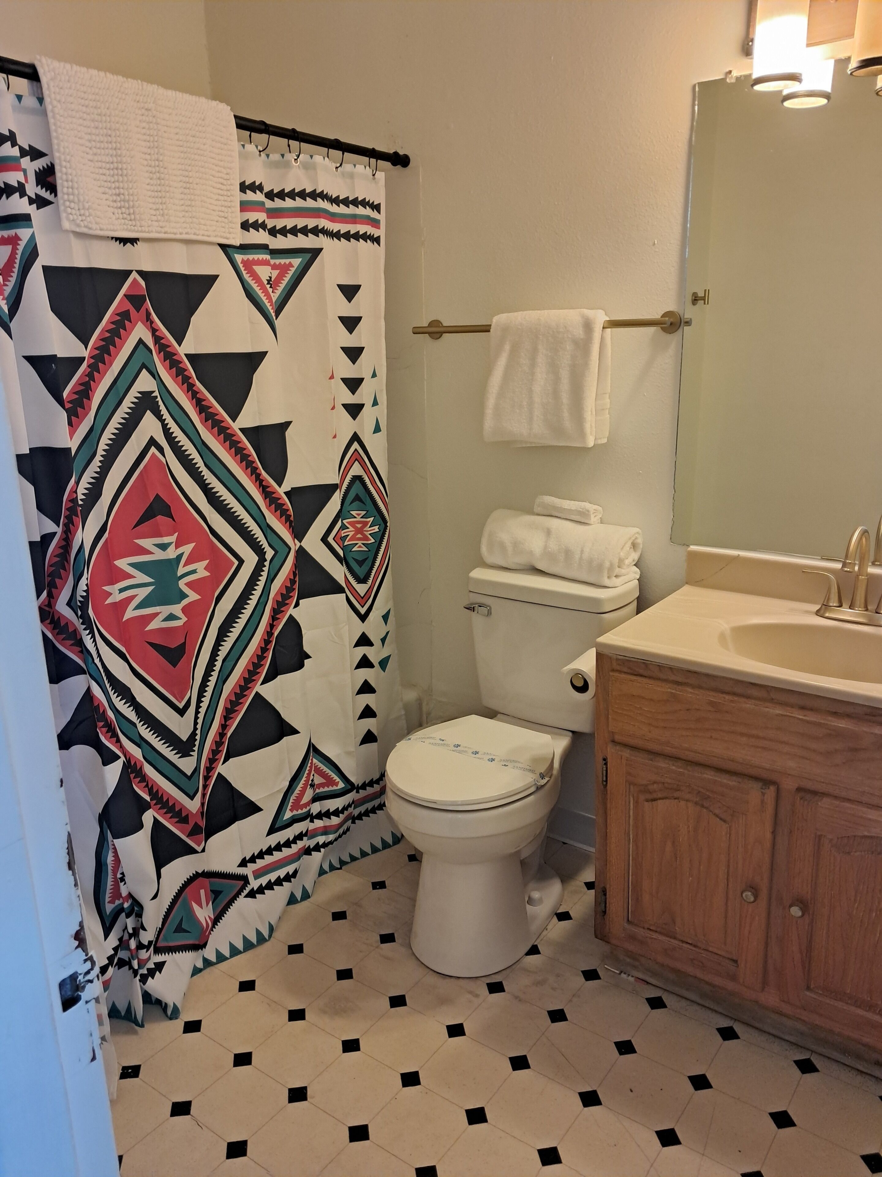 A bathroom with a patterned shower curtain, a toilet, a sink with a mirror, and a towel rack.