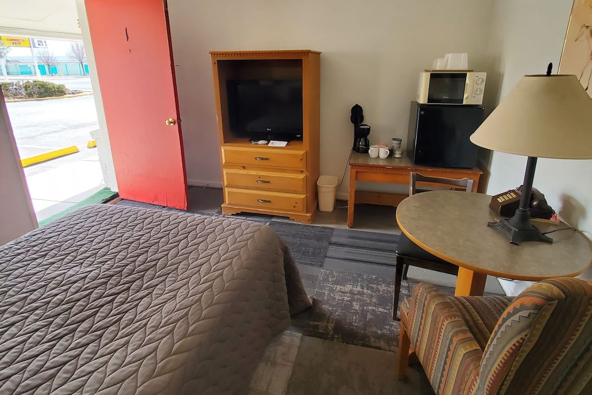 Una habitación de hotel con cama, televisor, escritorio con lámpara y microondas.