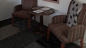 A room with two striped armchairs, a small wooden table with papers, and a mirror on the wall. - Southwest Motel (Grants)