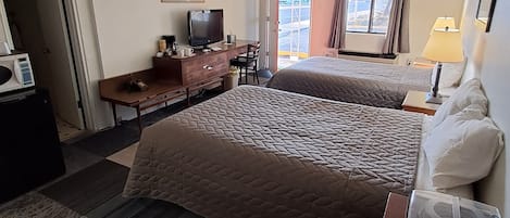 A hotel room with two beds, a desk with a television, a coffee maker, and a view of the outside.
