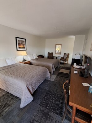 A hotel room with two beds, a desk, a chair, a television, and a framed picture on the wall. - Southwest Motel (Grants)