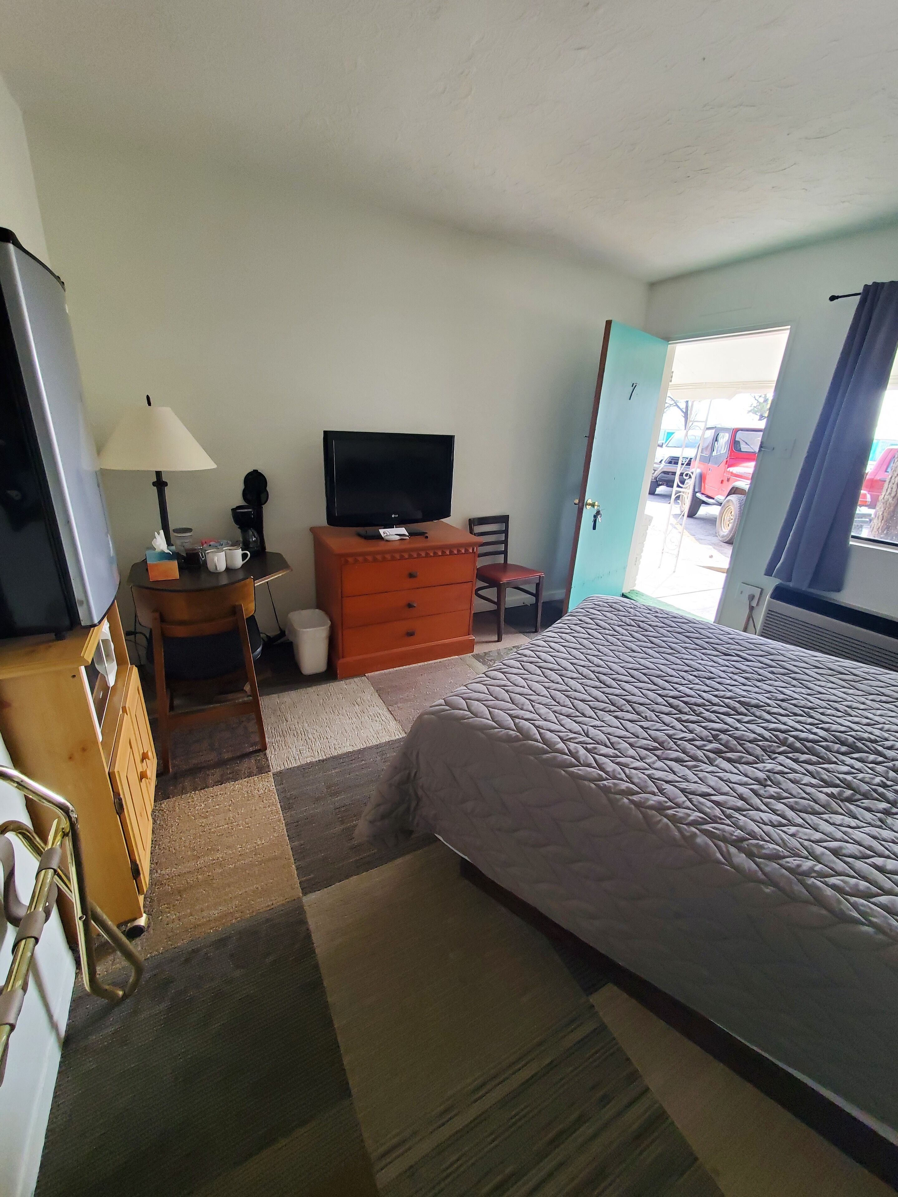 A hotel room with a bed, a television on a dresser, a chair, and a desk with a lamp.