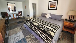 A bedroom with a bed, a desk, a chair, a mirror, and a framed picture on the wall. - Southwest Motel (Grants)