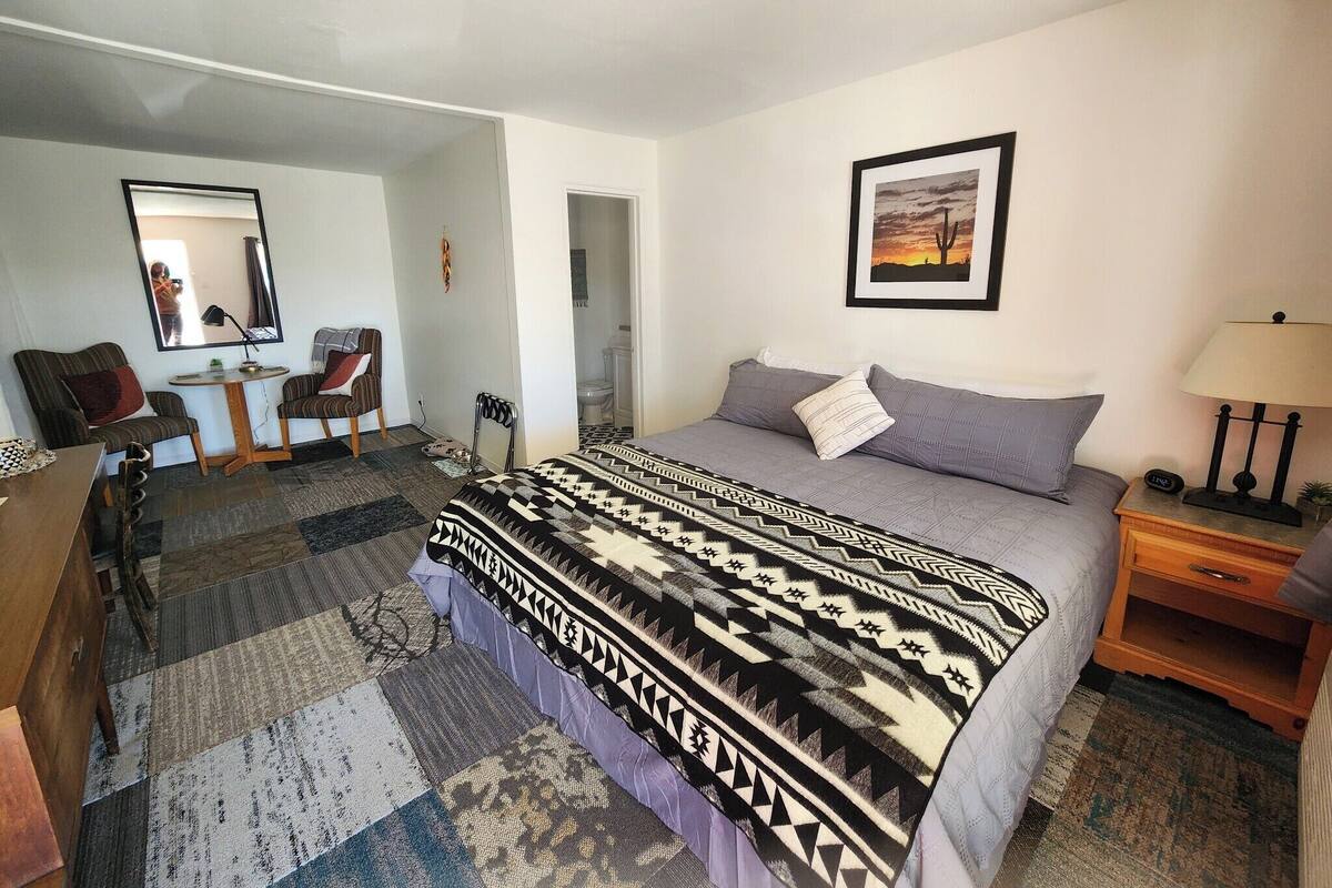 Un dormitorio con cama, escritorio, silla, espejo y un cuadro en la pared.