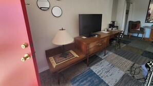 A hotel room with a wooden desk, a television, a lamp, and a patterned rug. - Southwest Motel (Grants)