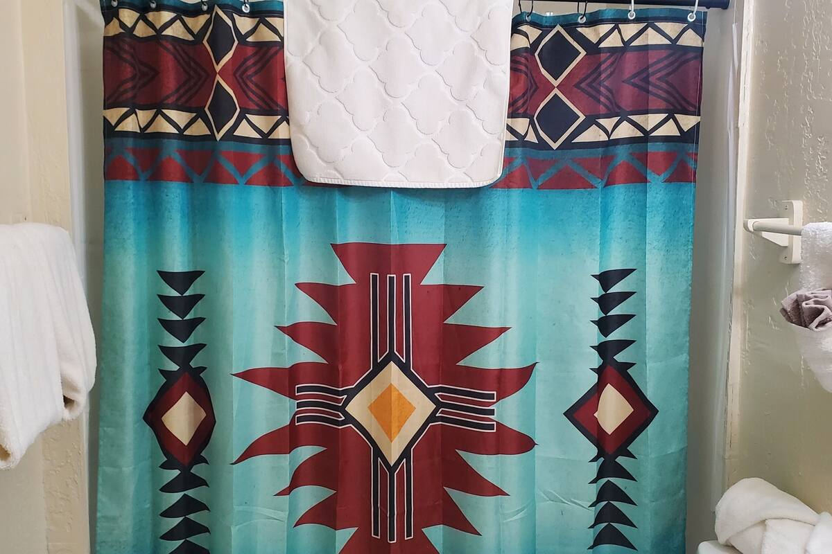 Un baño con cortina de ducha estampada con un diseño geométrico, una toalla blanca colgada en la barra de cortina y un inodoro con tapa blanca.