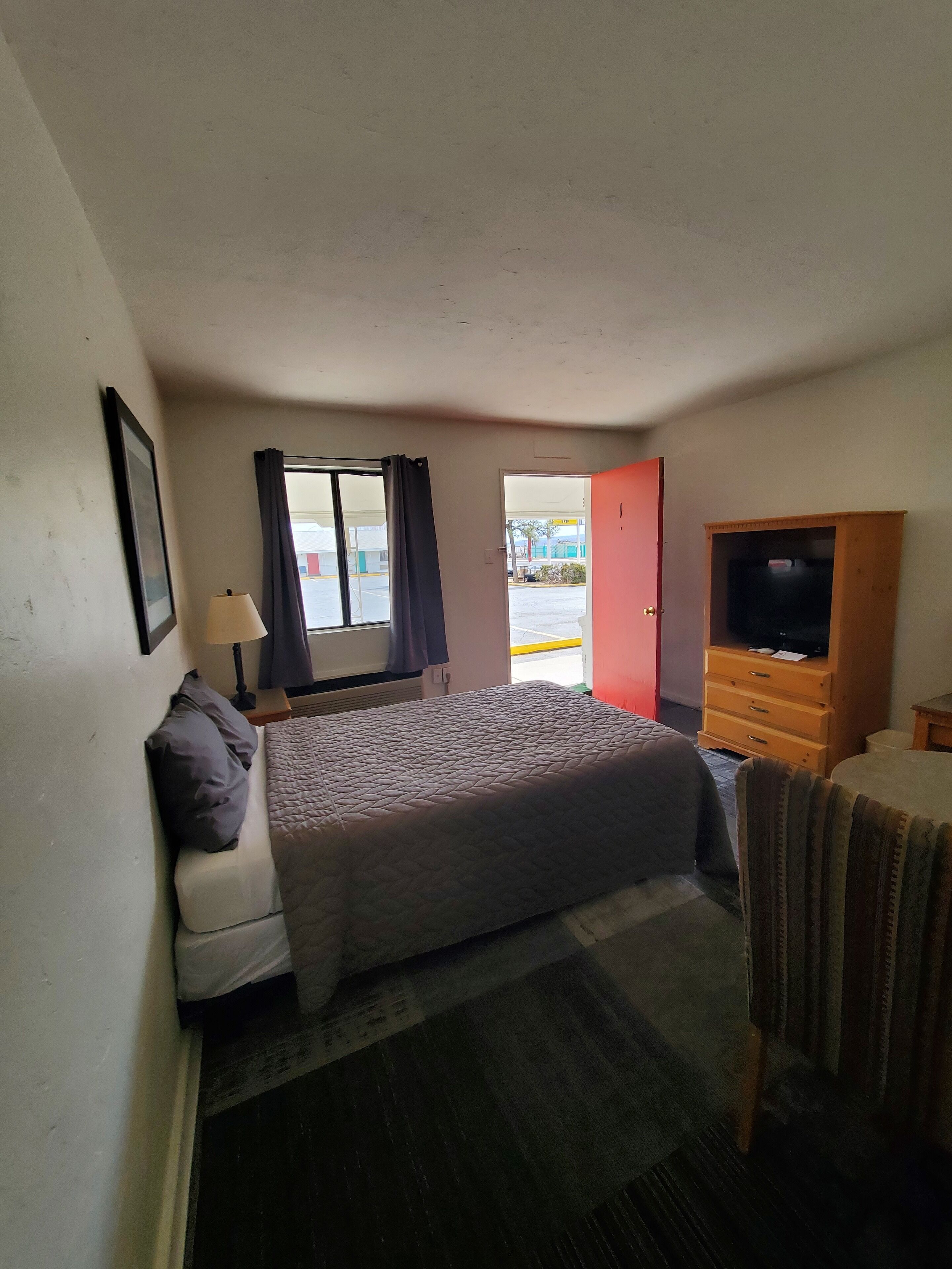 A hotel room with a bed, a TV cabinet, a lamp, and a window with curtains.