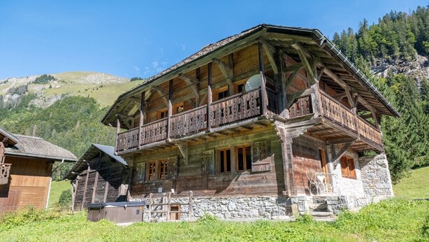 A wooden chalet with a balcony, stone foundation, and a mountainous backdrop. - Chalet Ski-In Plagnat, Ardent  (Montriond)