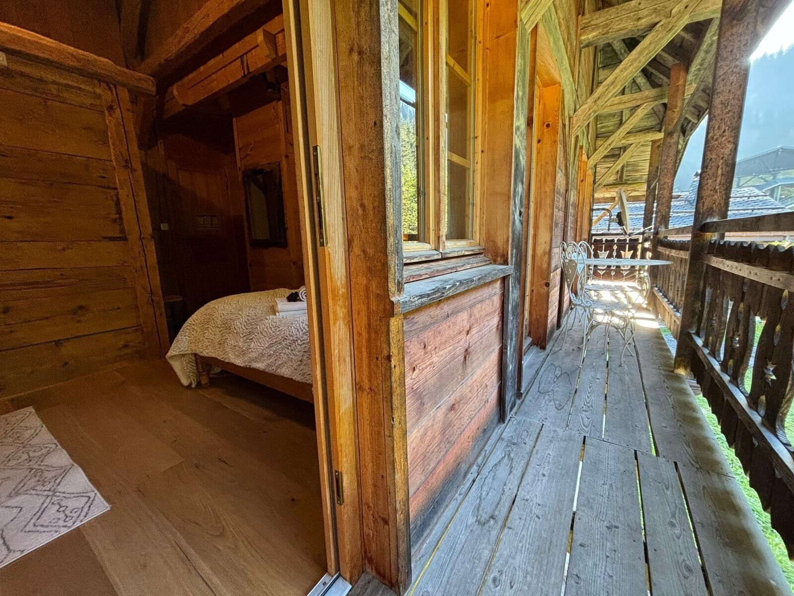 A wooden cabin with a bed, a window, and a wooden deck.