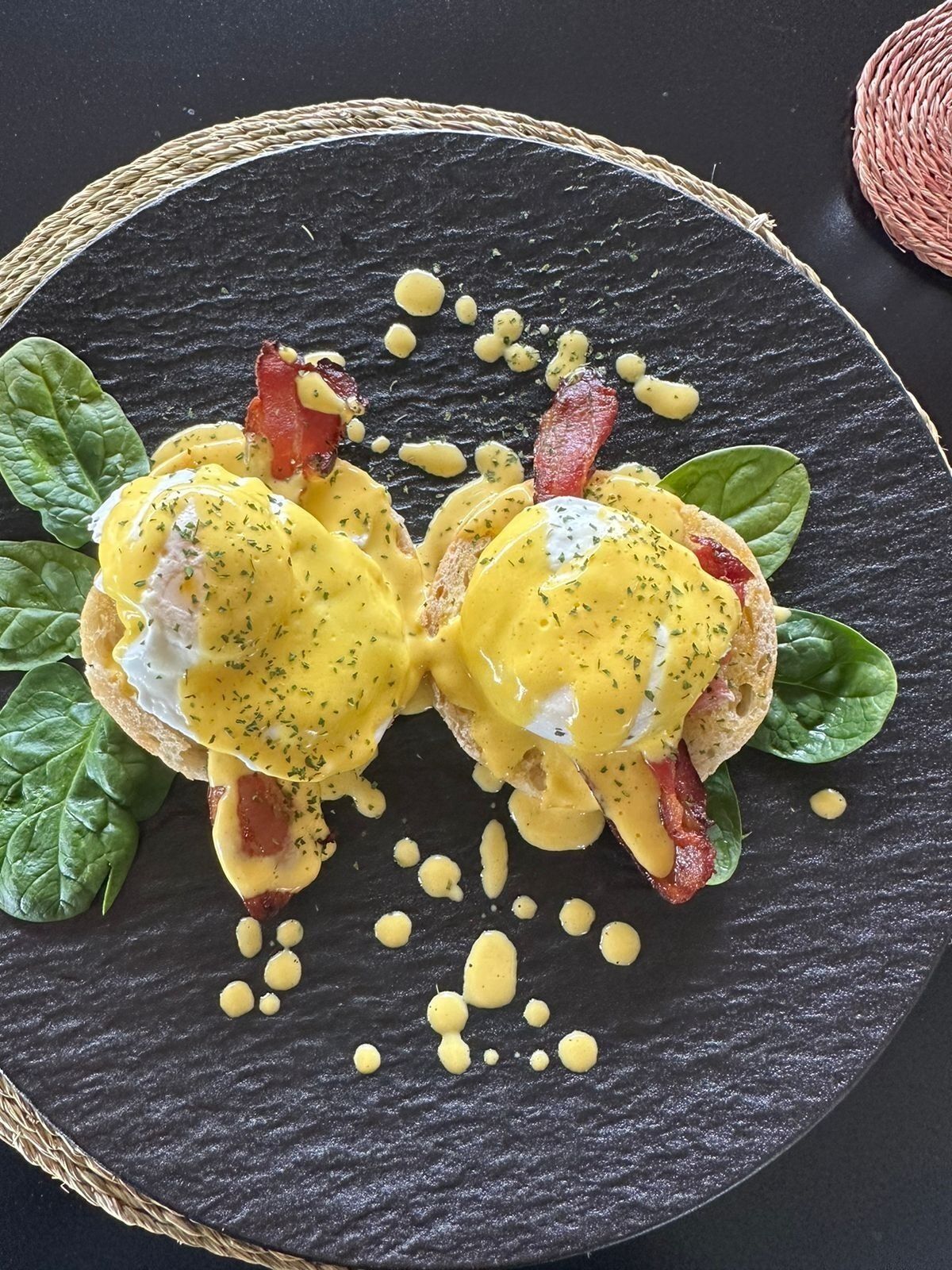 A breakfast dish with eggs, bacon, and spinach on a dark plate.