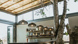 A modern bar area with a large tree trunk, wooden ceiling beams, and hanging pendant lights.