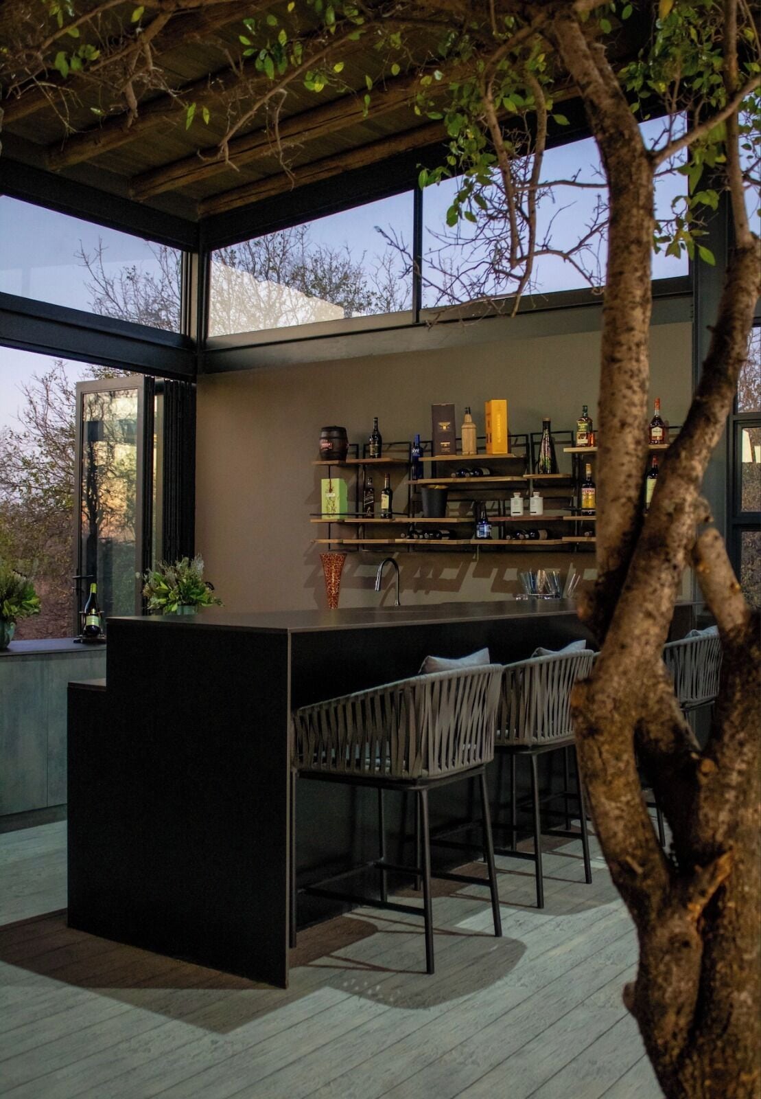 A modern outdoor bar area with a central island, bar stools, and shelves stocked with bottles.