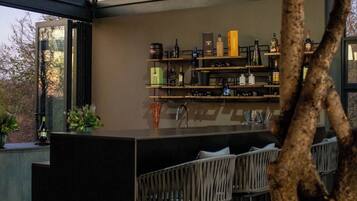 A modern outdoor bar area with a central island, bar stools, and shelves stocked with bottles.